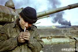Interior Ministry soldiers lights a cigarette. Smoke rises from the burning Steel Works behind him.